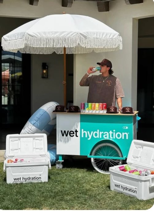 Man drinking beside a branded drinks trolley under a white parasol