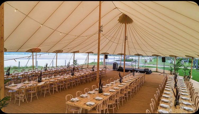 Long dining tables set under a sailcloth tent