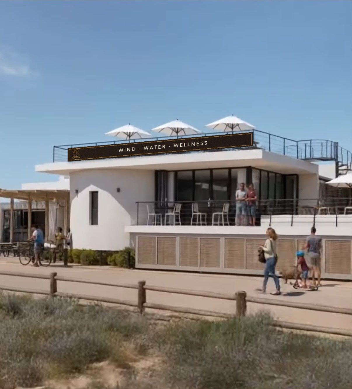 White beach clubhouse with an ORRA Wind Water Wellness banner on the rooftop railing